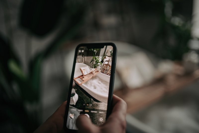Mans hand take photo by phone for social media luxury interior eco style bathroom with oval bathtub