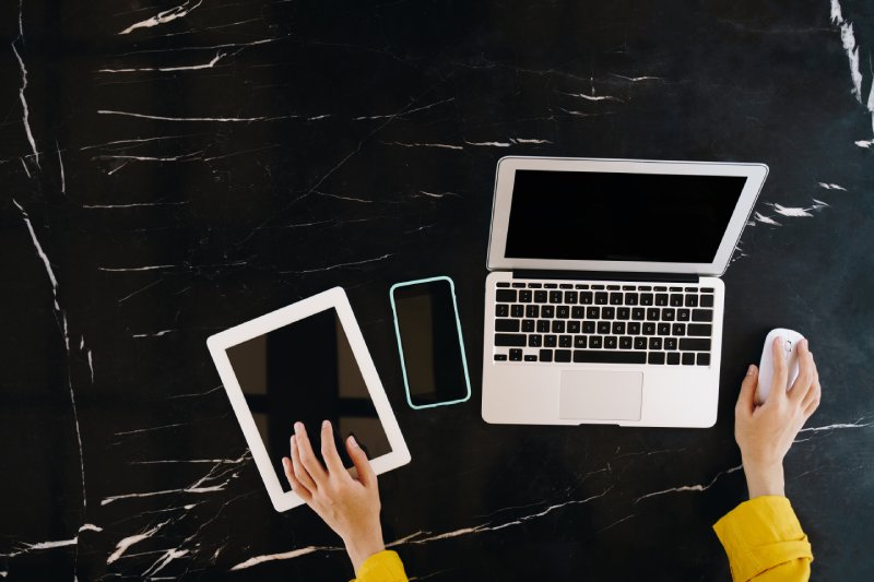 Closeup of hands using laptop, tablet and mobile with empty screen on black table. Technology concept.